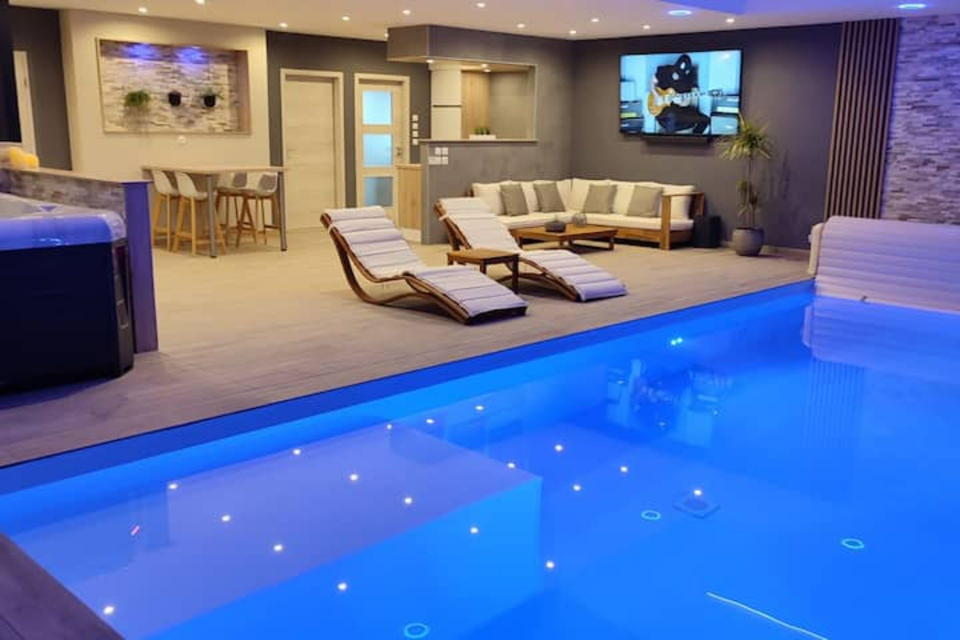 Ein moderner Poolbereich im Innenbereich mit Liegestühlen und einem an der Wand befestigten Fernsehbildschirm.