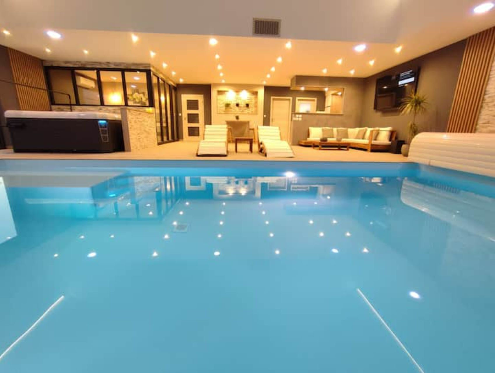 Una piscina interior con jacuzzi, sillas de descanso y una cama balinesa.