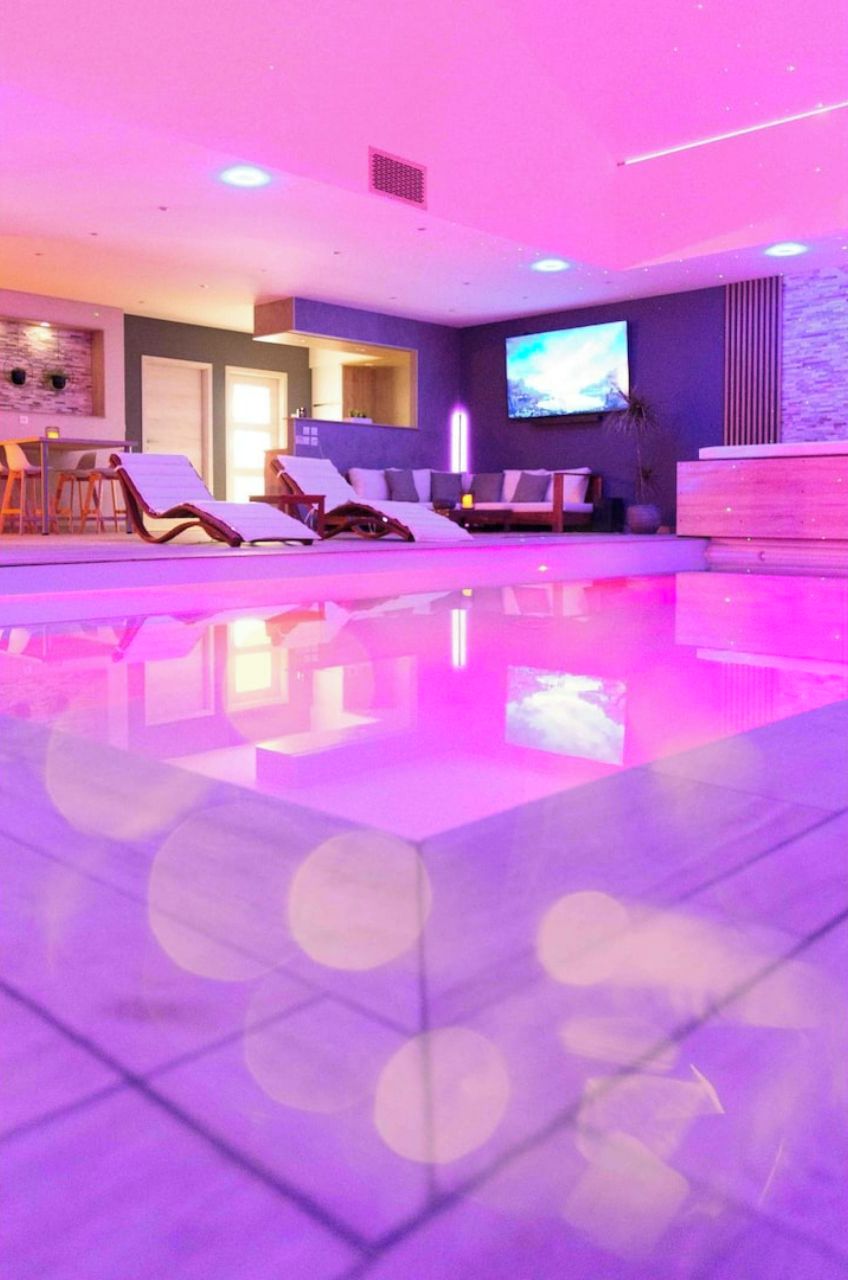 A modern indoor pool area with lounge chairs and a flat-screen TV.