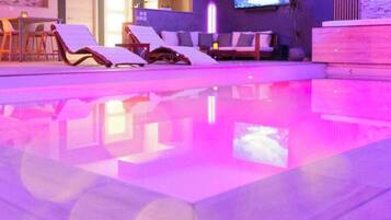 A modern indoor pool area with lounge chairs and a flat-screen TV.