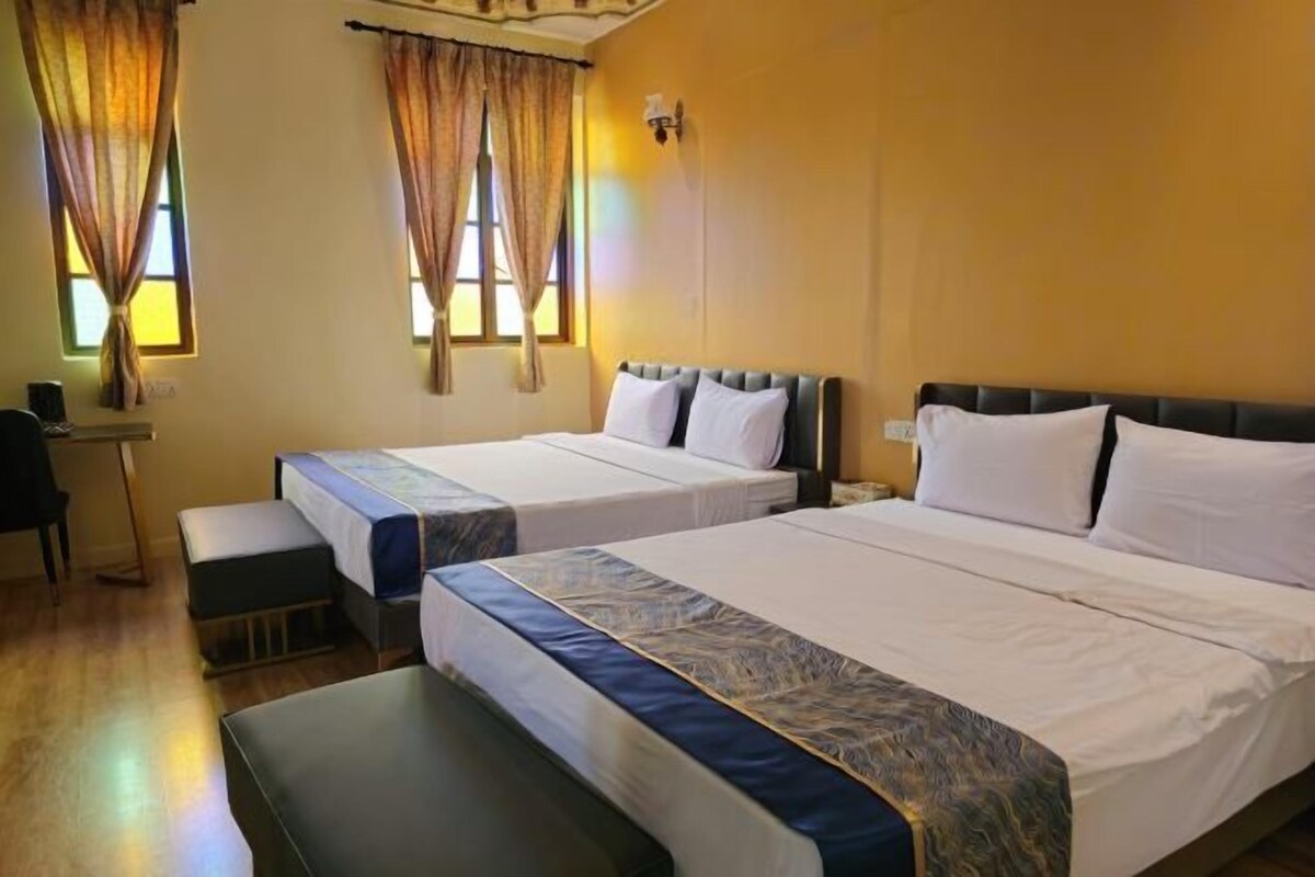 A hotel room with two beds, a desk, and a bench.