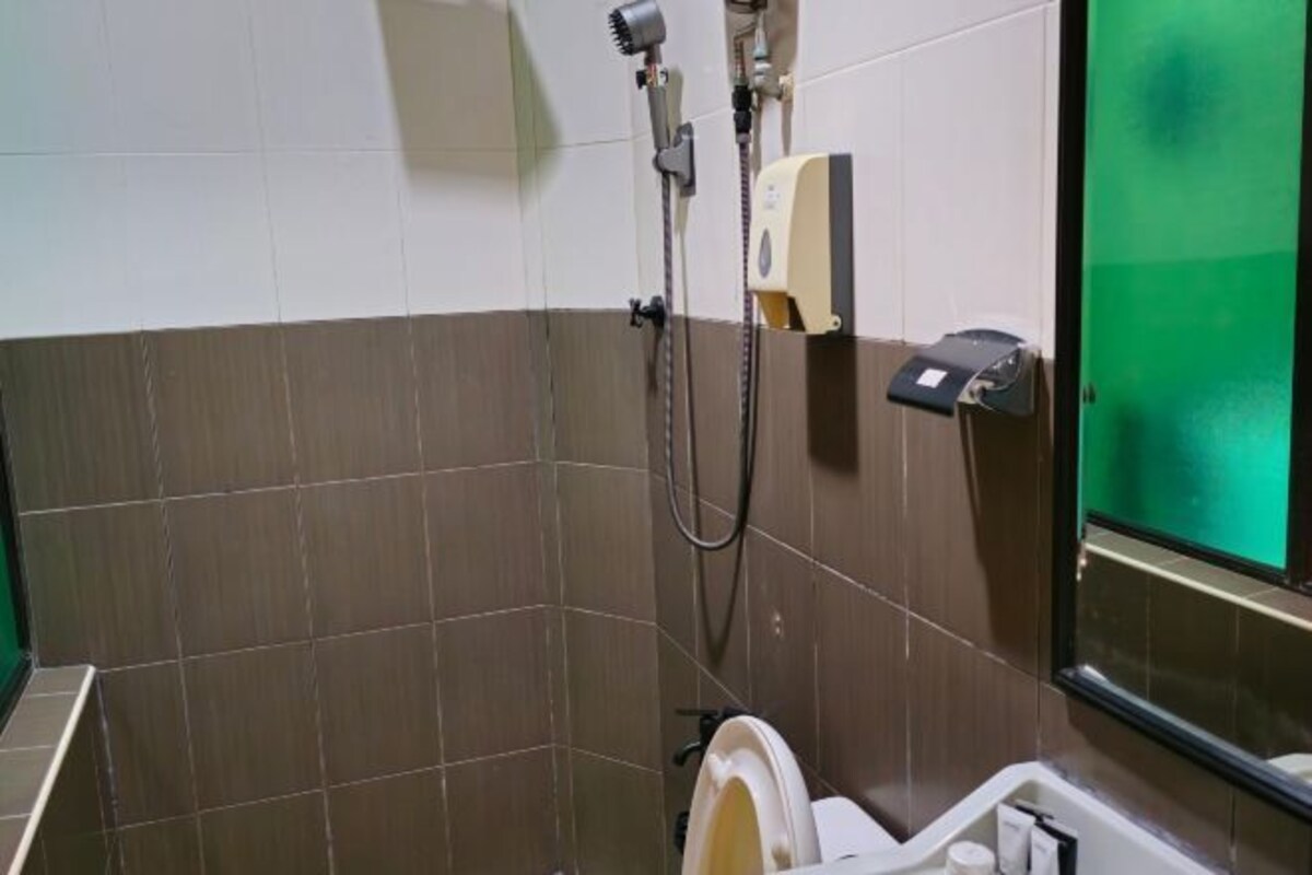 A bathroom with a toilet, a hand dryer, and a shower head.