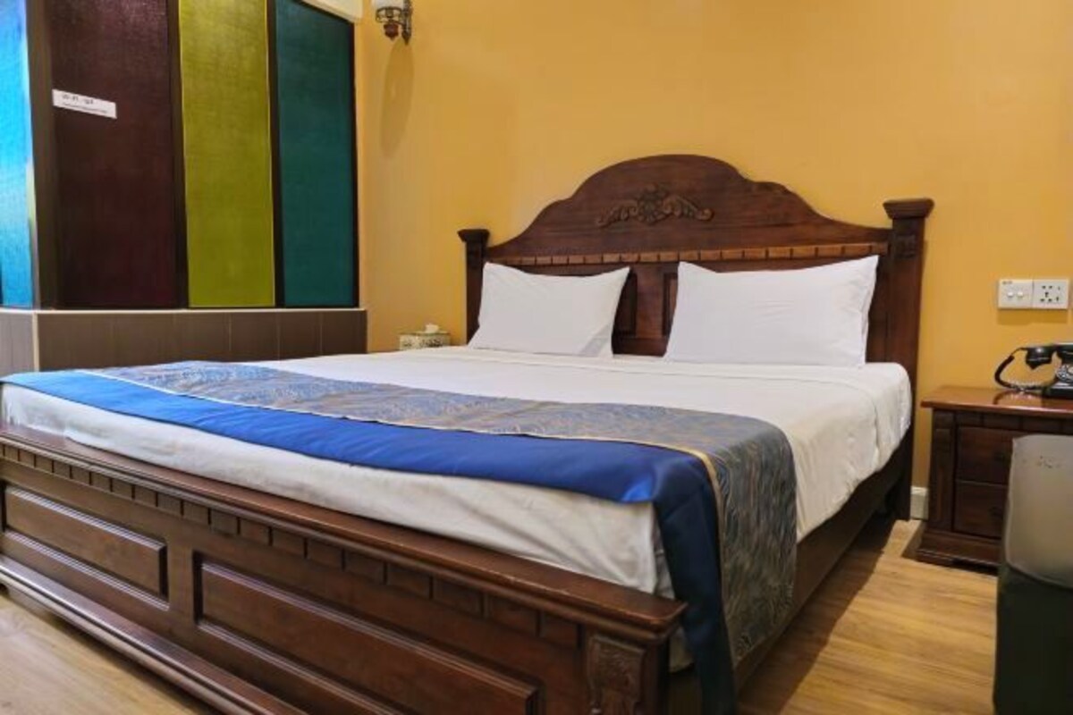 A neatly made bed with a wooden headboard, a bedside table with a lamp, and a wall with a color-coded door.
