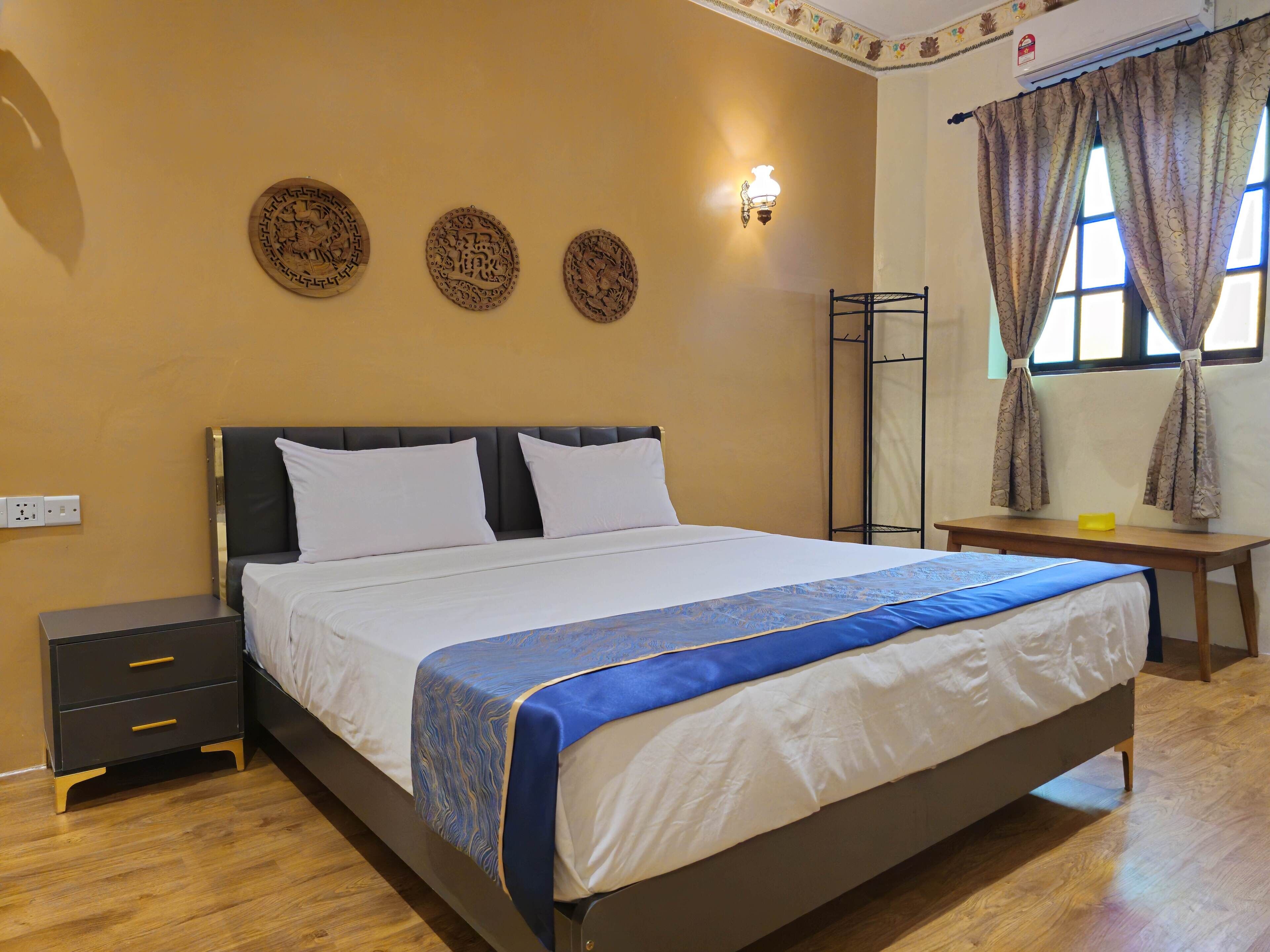 A neatly made bed with a blue and white bedspread, a bedside table with a lamp, and a wall-mounted air conditioning unit.