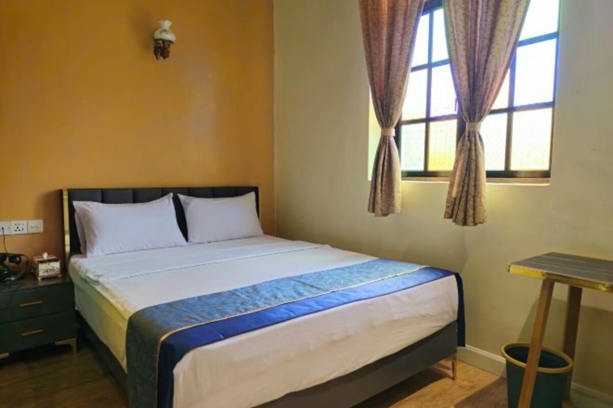 A hotel room with a bed, a nightstand, a small table, and a window with curtains.