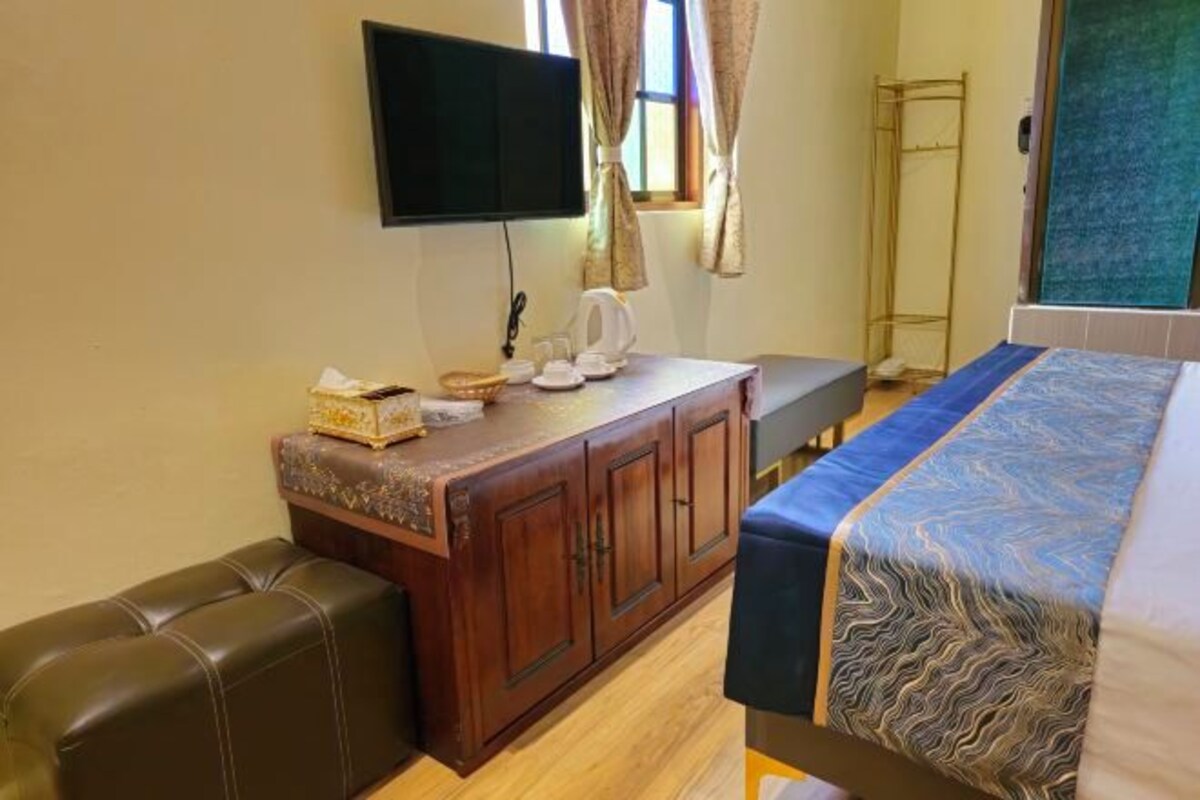 A hotel room with a bed, a wooden dresser, a television, and a window with curtains.