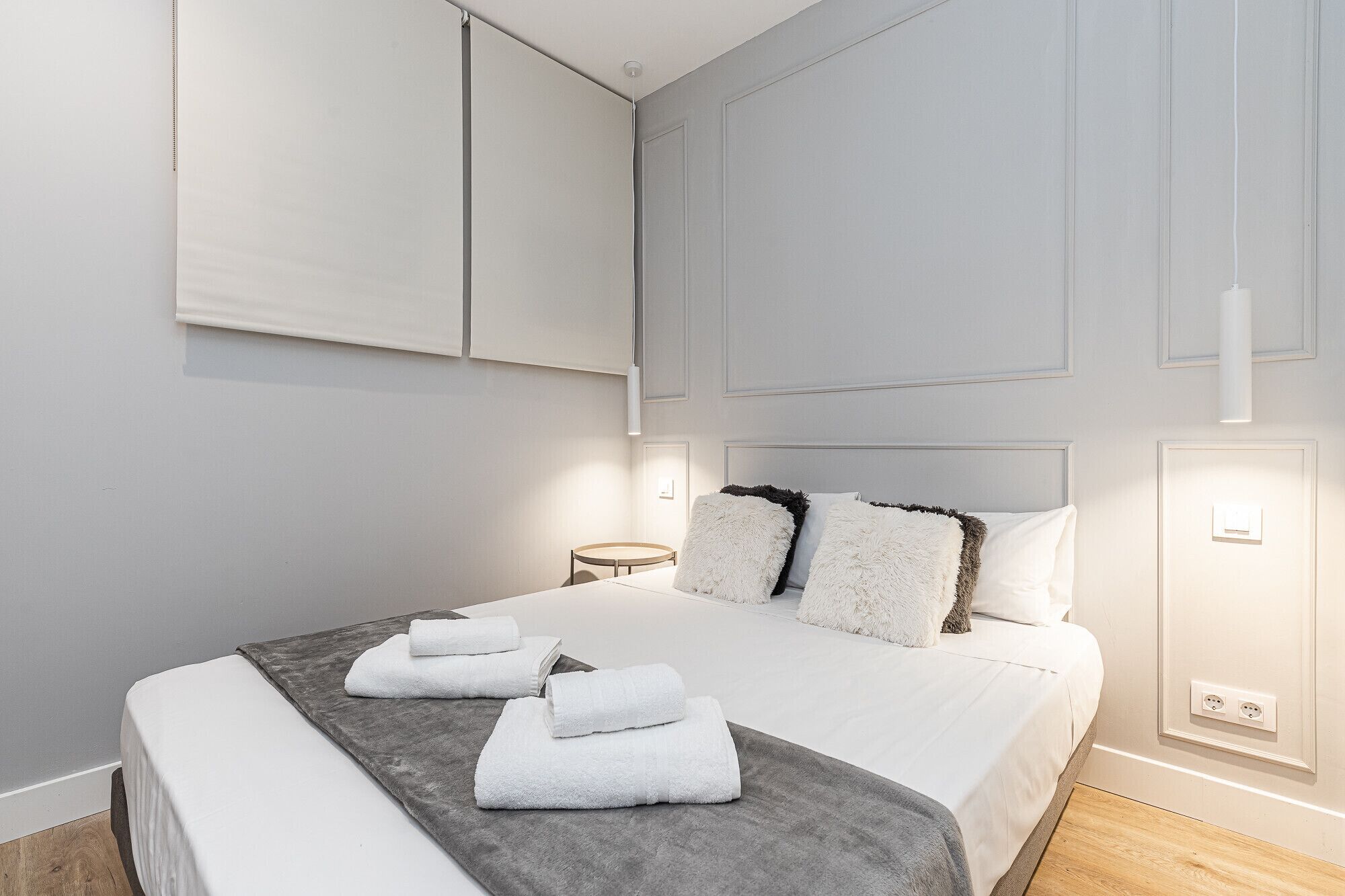 Een moderne slaapkamer met een groot bed, witte beddengoed en een grijs vloerkleed.