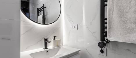 A modern bathroom with a white marble sink, a round mirror, and a towel rack.