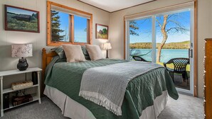 Ein Schlafzimmer mit einem großen Bett, zwei Fenstern, Blick auf einen See und einem Sessel am Fenster.