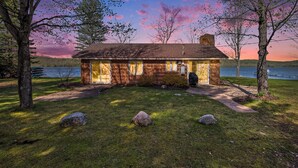 Eine Holzhütte mit Steinverkleidung, einer Veranda und Blick auf einen See bei Sonnenuntergang.