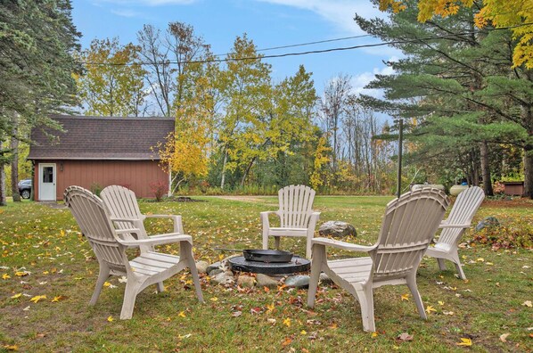 A backyard with four Adirondack chairs arranged around a circular fire pit. - Welcome to the Loon Lodge on Intermediate Lake! (Bellaire)
