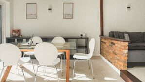 A modern dining area with a glass table, white chairs, and a brick accent wall. - Idyllic Home in Picturesque Village of Wraysbury - Pass the Keys (Wraysbury)