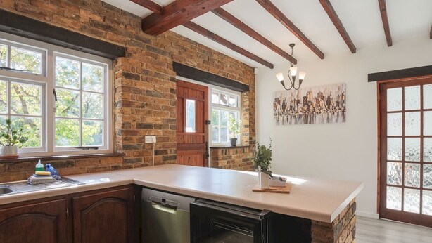 A kitchen with exposed brick walls, wooden beams, a dishwasher, and a large window. - Idyllic Home in Picturesque Village of Wraysbury - Pass the Keys (Wraysbury)