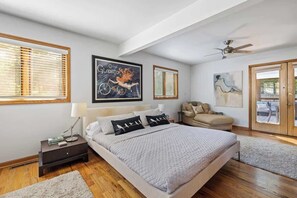 Une chambre à coucher comprenant un lit, des tables de chevet, un canapé, un ventilateur de plafond et des œuvres d’art accrochées aux murs.