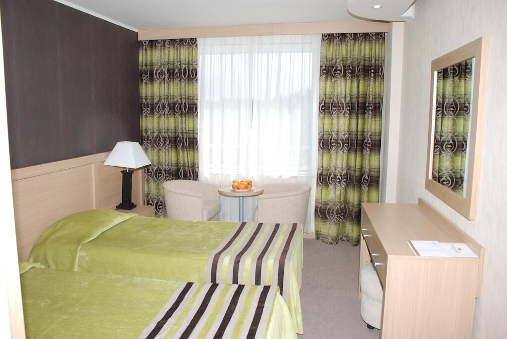 A hotel room with a bed, a desk, a chair, a lamp, and a window with curtains.