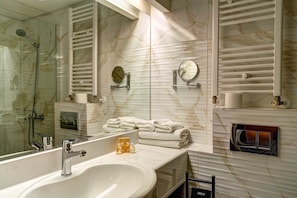 A modern bathroom with a large mirror, a glass-enclosed shower, and a marble-tiled wall.