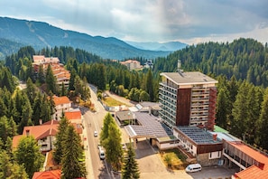 A hotel with a modern design, surrounded by a forested mountain landscape.