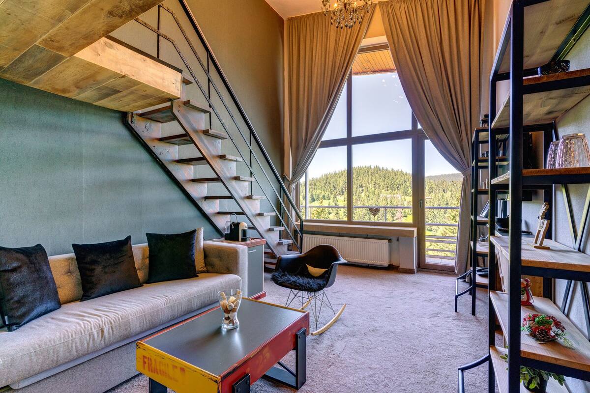 A modern living room with a sofa, a coffee table, a rocking chair, and a staircase leading to a balcony.
