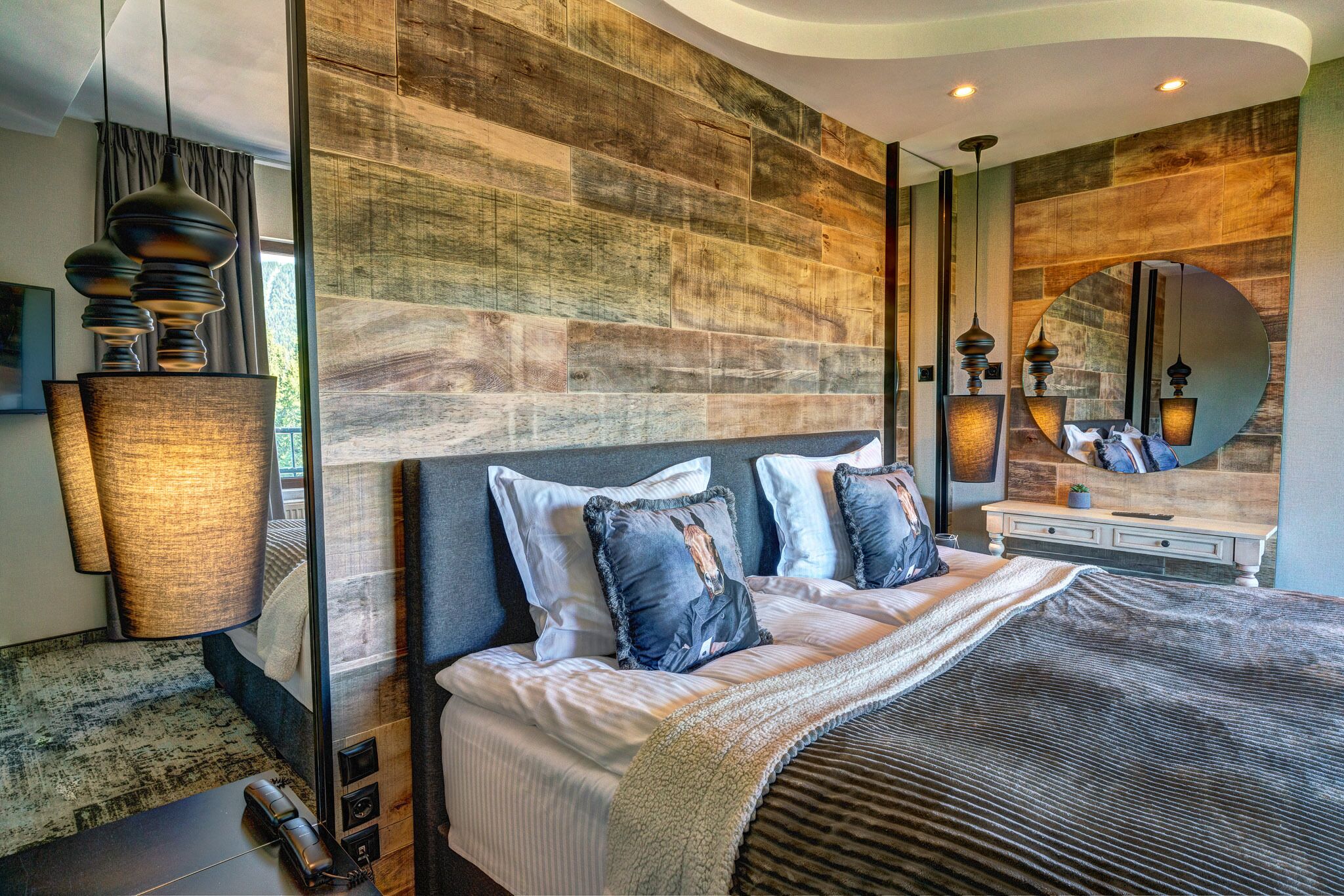 A modern bedroom with a large bed, a wooden accent wall, and a mirror above the bed.