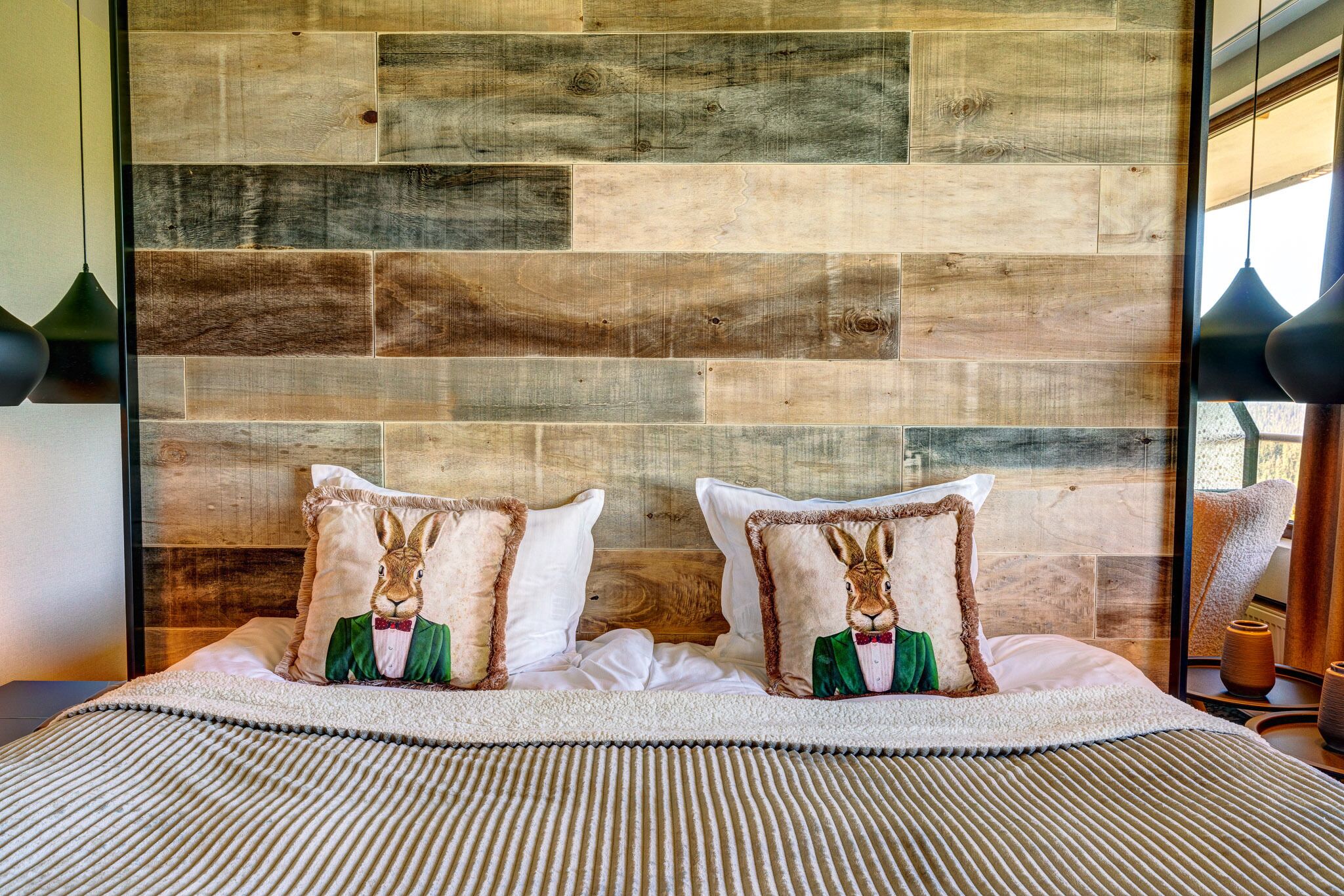 Una cama con cabecera de madera, dos almohadas con motivos de conejos y una manta a rayas.
