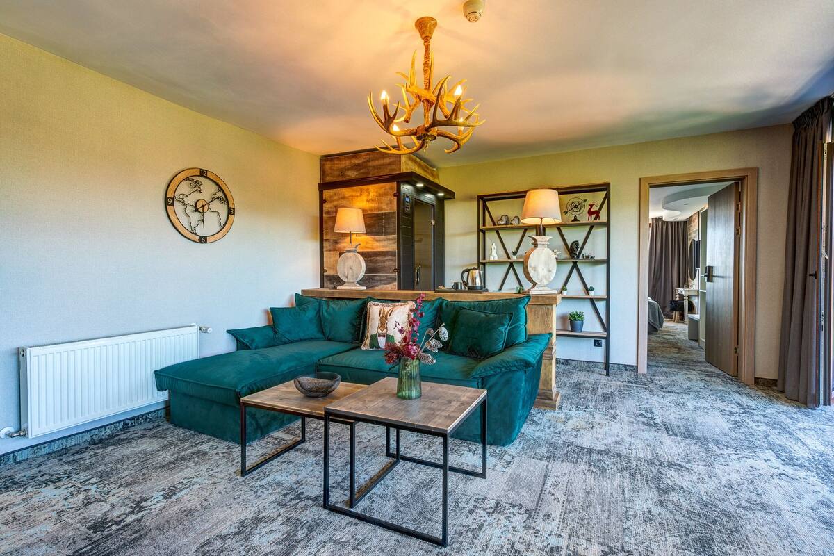 A living room with a green sofa, a wooden coffee table, a chandelier, a world clock, and a bookshelf.
