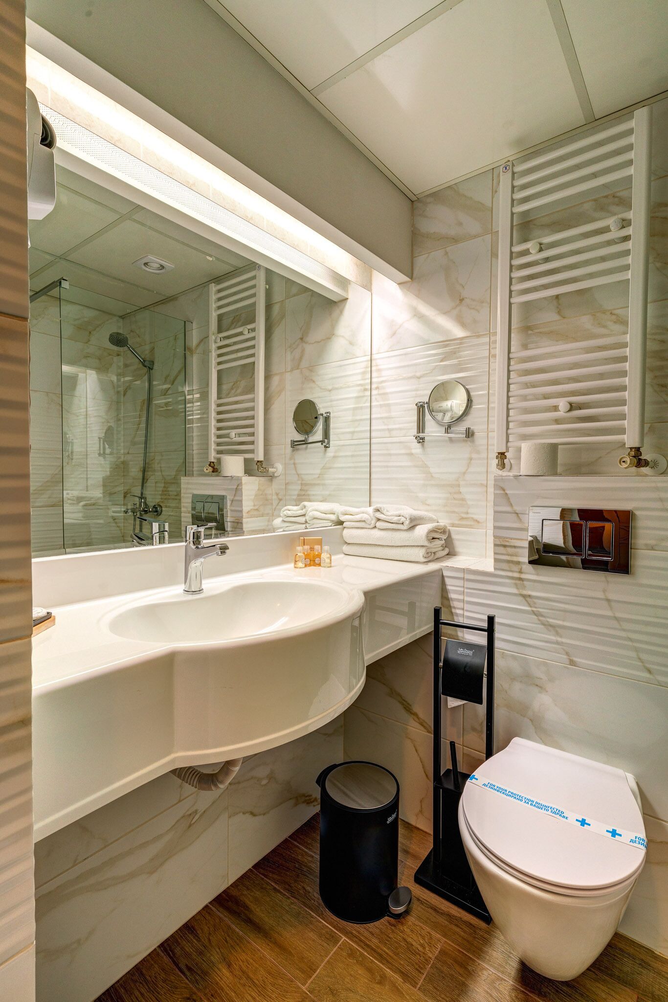 A modern bathroom with a large mirror, white sink, and a toilet.