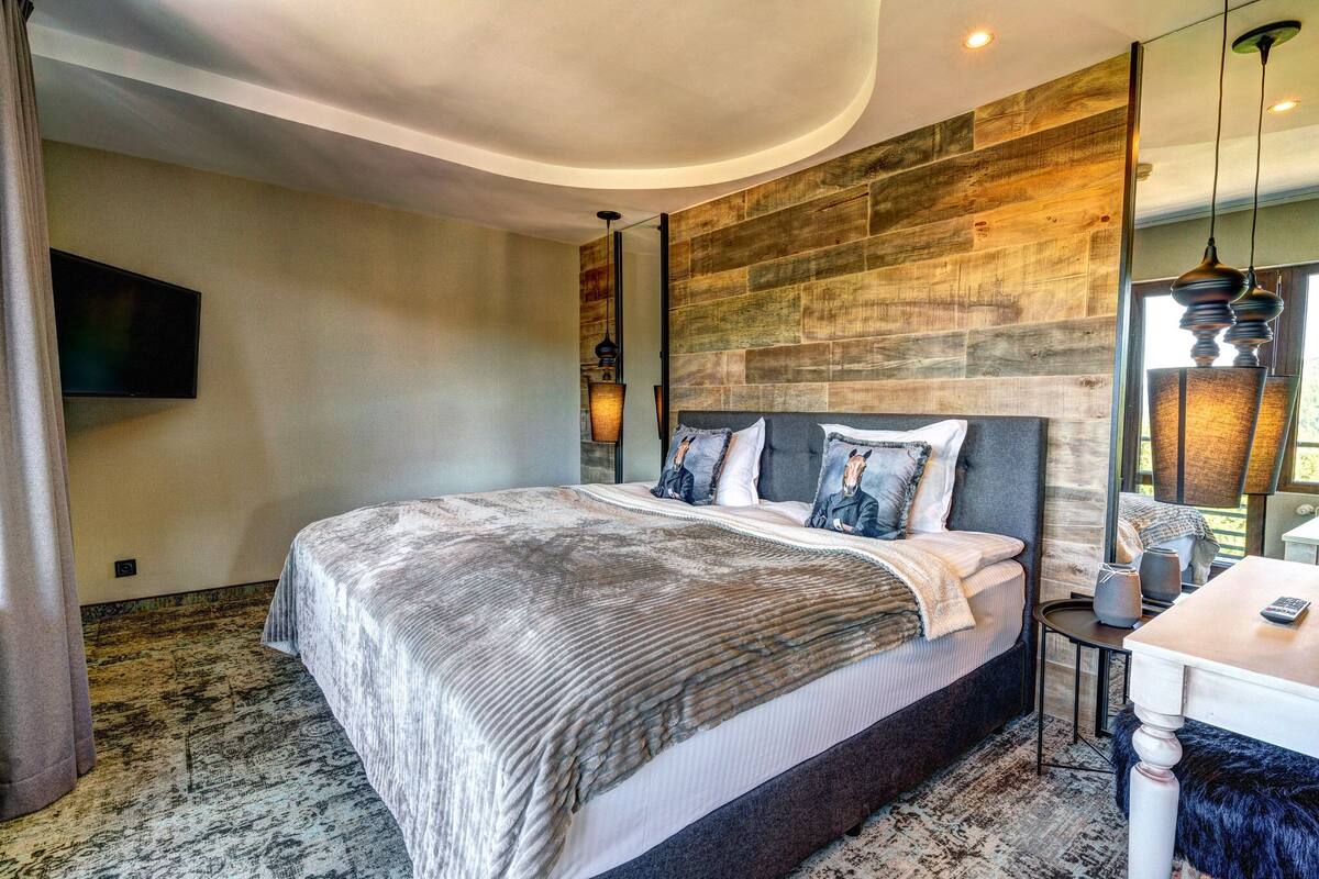 A modern bedroom with a large bed, a flat-screen TV mounted on the wall, and a wooden accent wall.