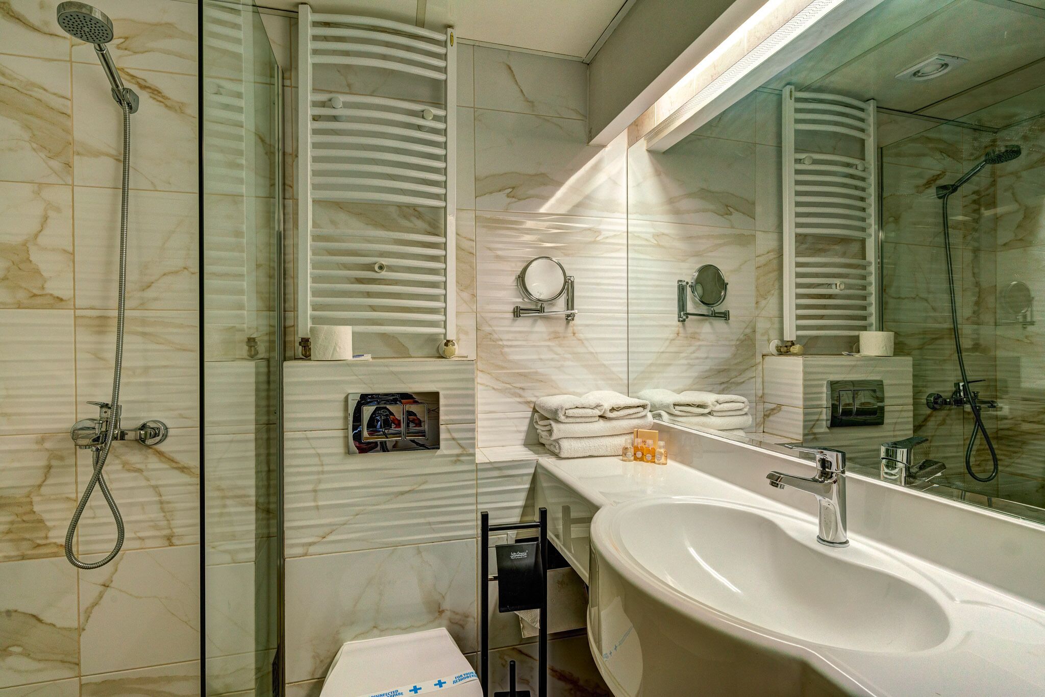 A modern bathroom with a large sink, a shower with a handheld showerhead, and a towel rack.