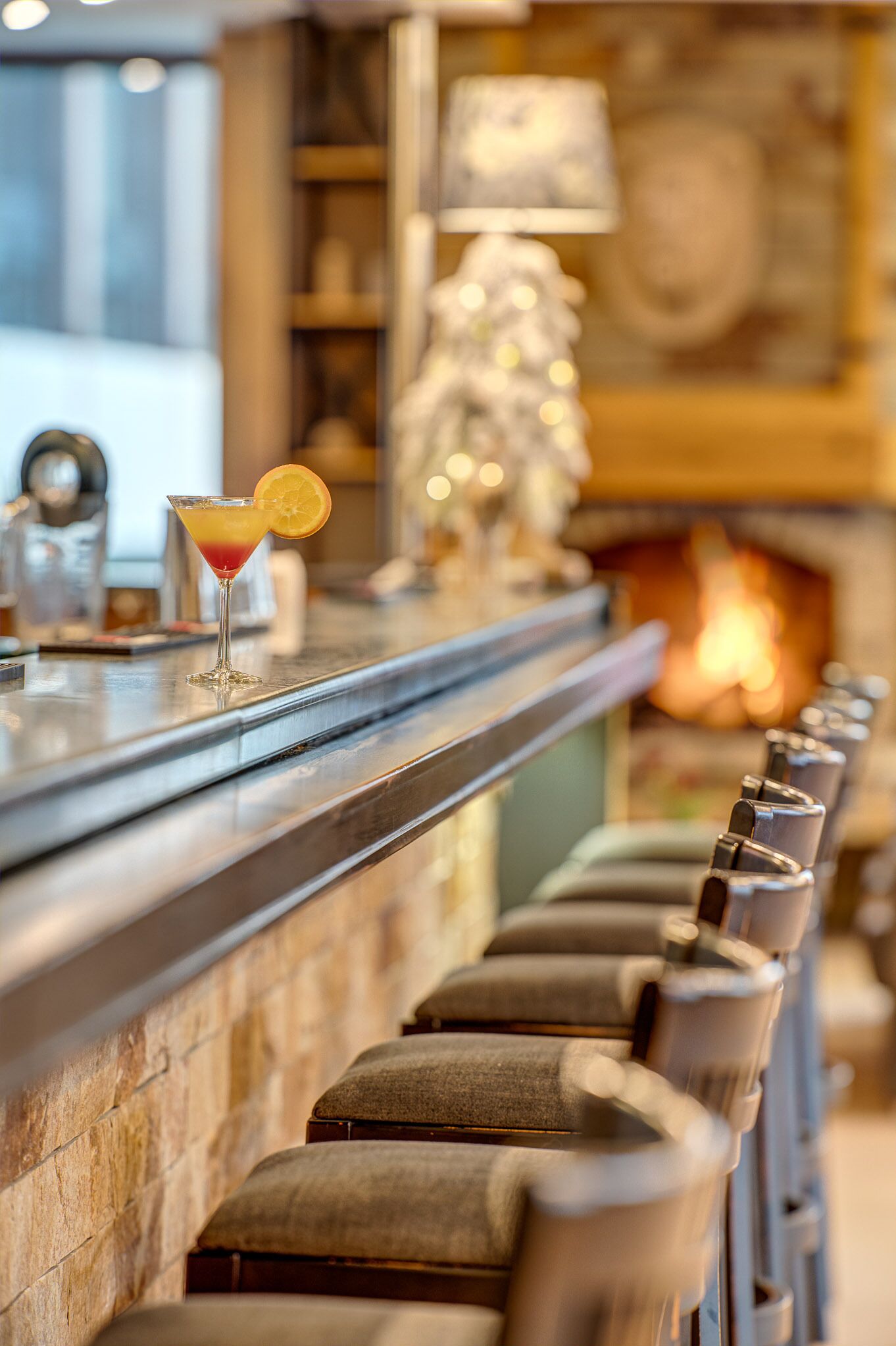 Zona de bar con un cóctel, una chimenea y taburetes acolchados.