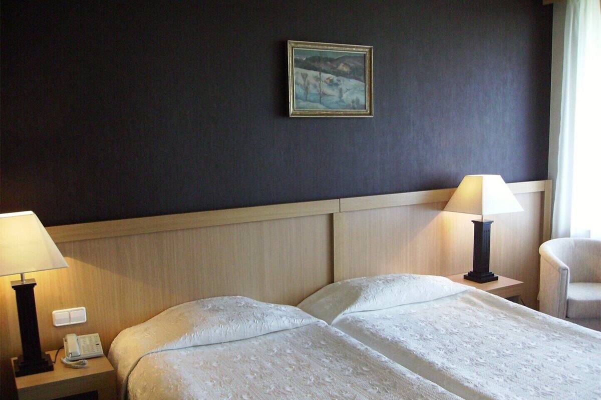 A hotel room with two beds, bedside lamps, a painting on the wall, and a chair.