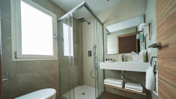 Un baño moderno con ducha vidriada, inodoro, tocador con espejo y ventana que proporciona luz natural.