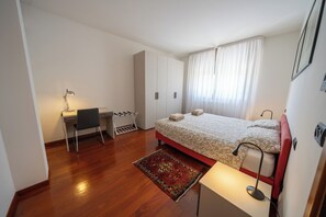 Un dormitorio con cama, escritorio con silla, armario y ventana con cortinas.