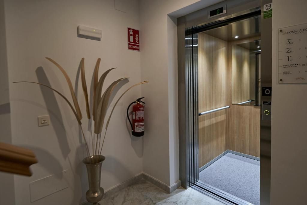 Un ascensor de hotel con un extintor de incendios fijado a la pared, un cartel de salida de incendios y un plano de planta.