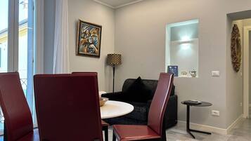 A modern living room with a black sofa, red chairs, a small round table, and a painting on the wall.
