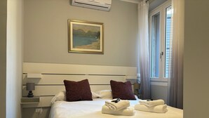 Ein Hotelzimmer mit einem großen Bett, zwei Kissen, einem Bild an der Wand, einem Fenster mit Vorhängen und einem Nachttisch mit einer Lampe.