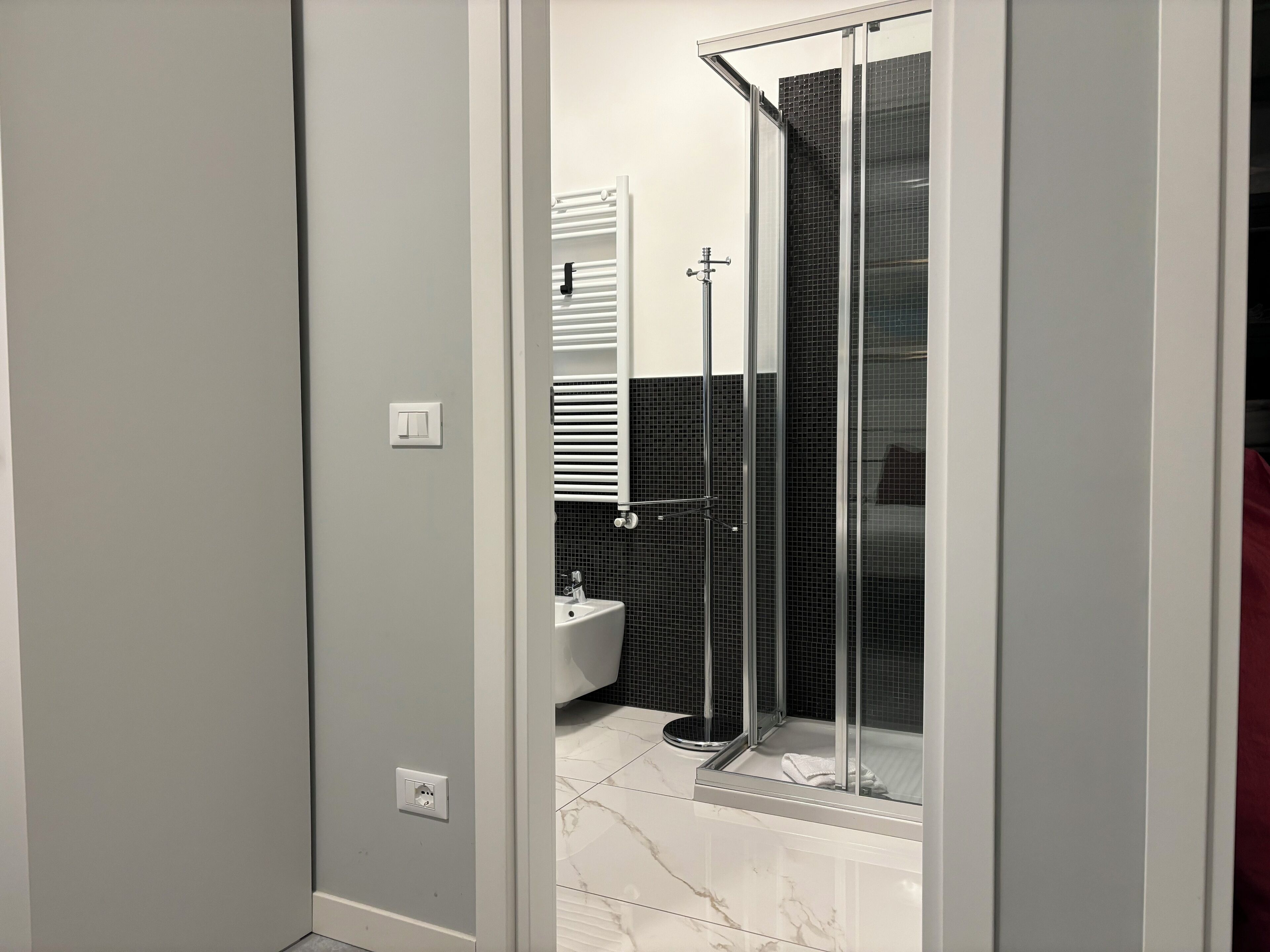 A modern bathroom with a glass-enclosed shower, a white sink, and a black tiled wall.