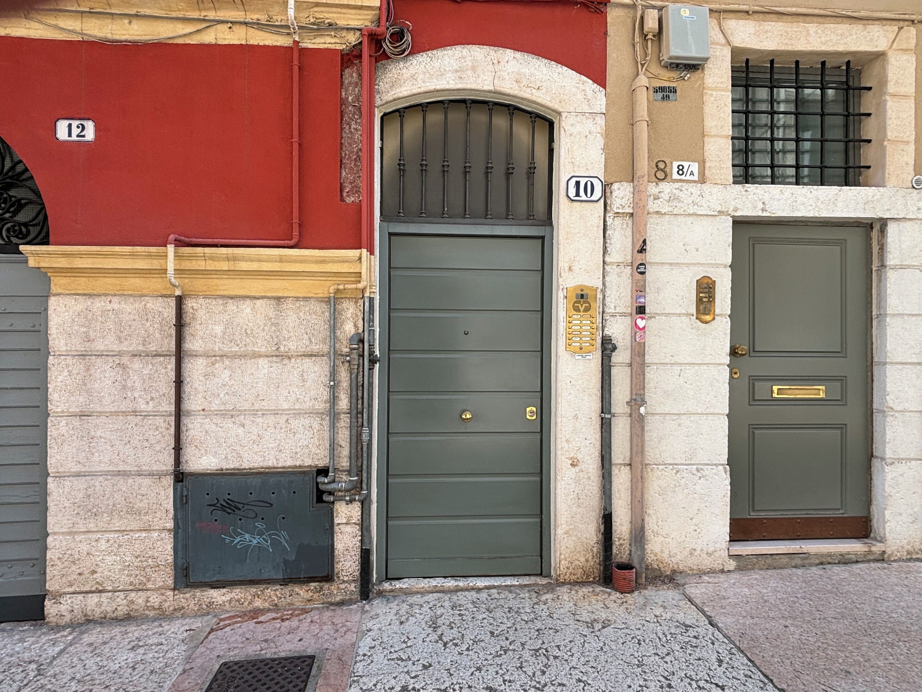 A building facade with numbered doors, a metal gate, and a small trash bin.