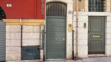 A building facade with numbered doors, a metal gate, and a small trash bin.
