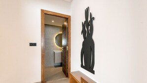A hallway with a wooden door leading to a bathroom, a glass bench, and a wall-mounted abstract sculpture. - Paul Verlaine  (La Marsa)