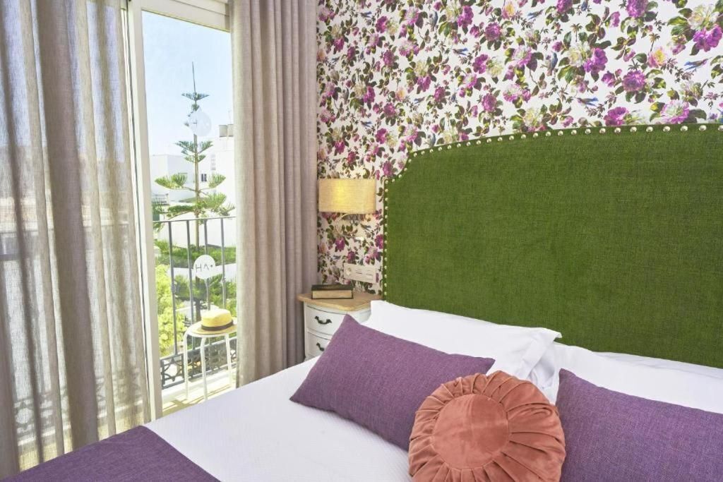 A hotel room with a large bed, a green headboard, and a floral-patterned wall.