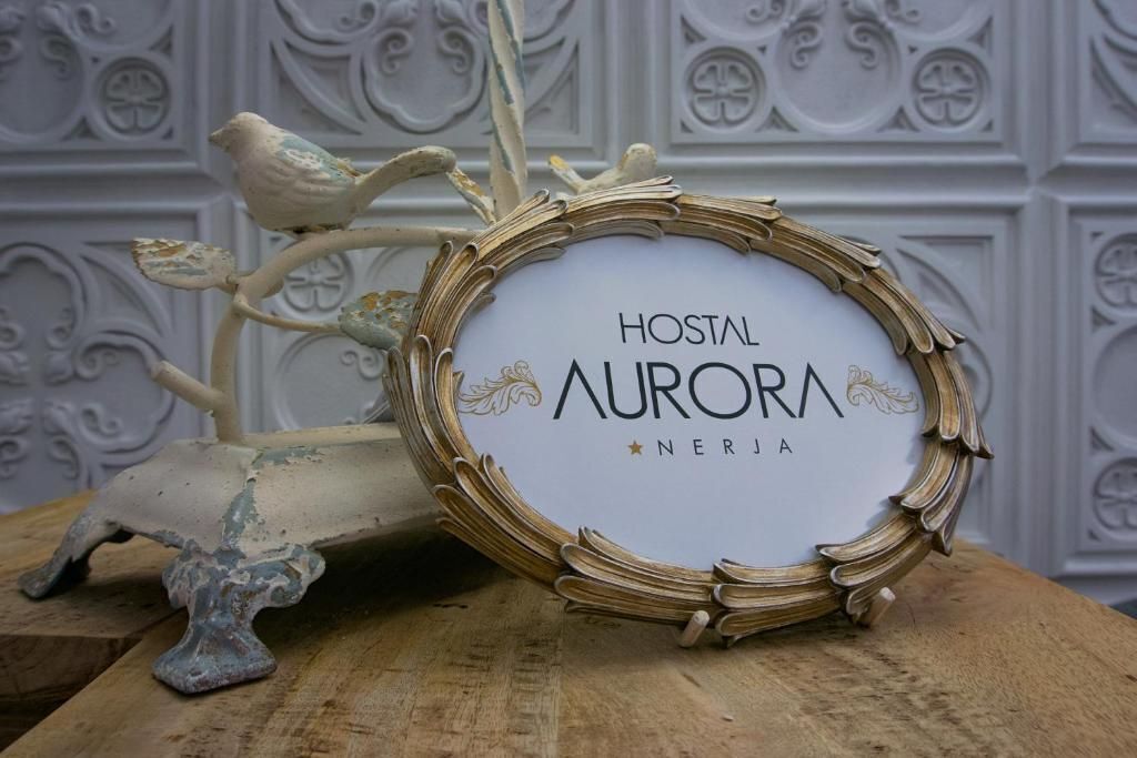 A framed sign with the text "HOSTAL AURORA NERJA" on a wooden surface.