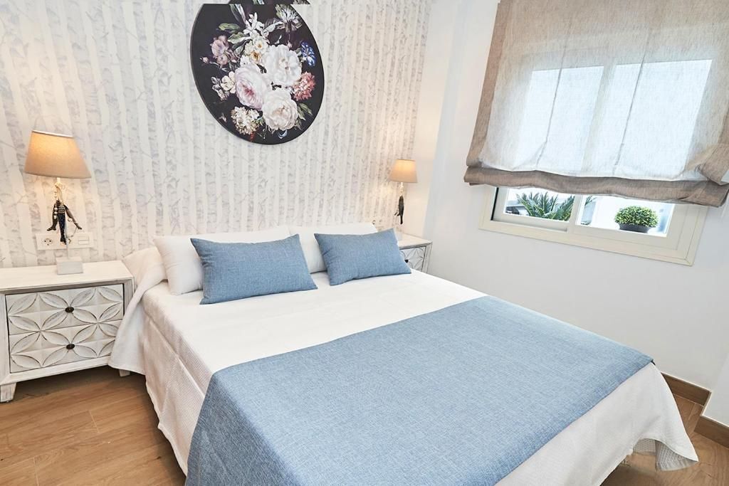 Un dormitorio con una cama, dos mesitas de noche, un reloj de pared, una ventana con vistas y una obra de arte floral.