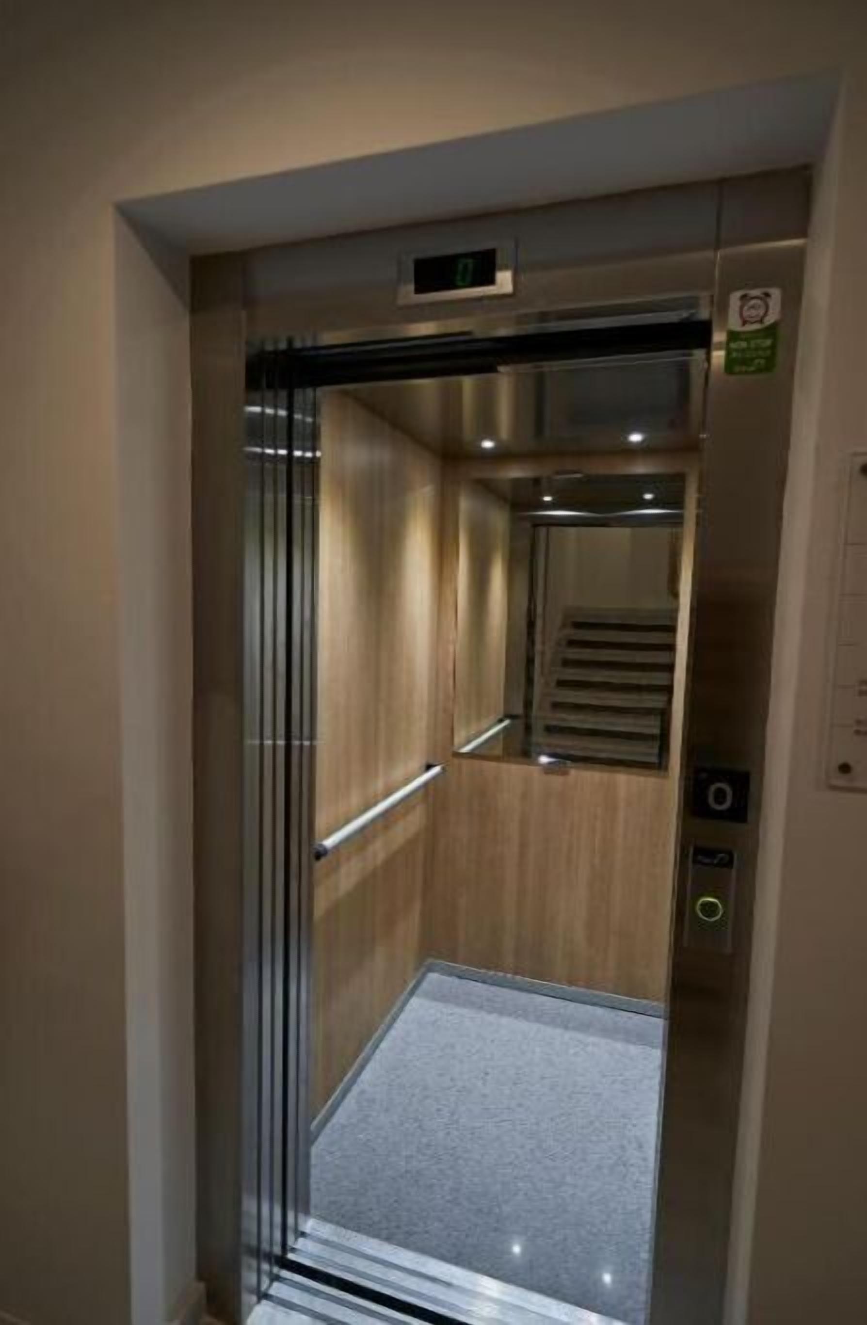 Un ascenseur moderne doté d’un écran numérique, d’un intérieur en bois et d’une rampe métallique.