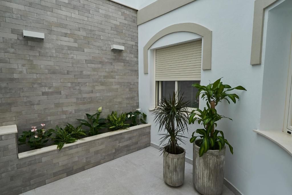 Un interior moderno con una pared de ladrillo gris, una ventana con persiana color crema y dos grandes macetas con plantas.