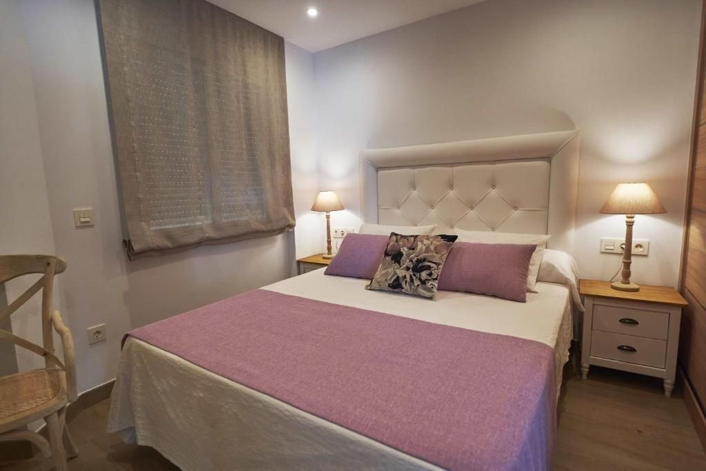 Un dormitorio con una cama grande, dos mesitas de noche, una silla y una ventana con cortinas.