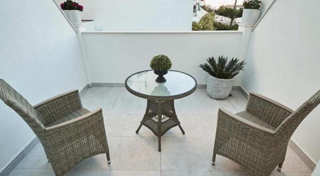 A balcony with two wicker chairs, a glass table, and potted plants.