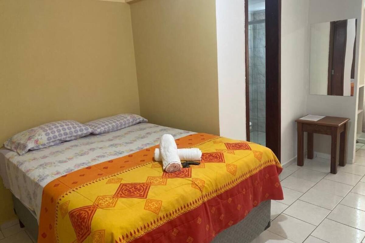 A hotel room with a bed, a small table, and a mirror.