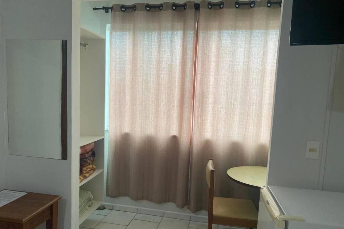 A room with a bed, a small table, a chair, and a shelf with folded clothes.