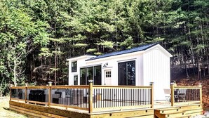 Une petite cabane à un seul étage, dotée d’une terrasse et entourée d’une forêt dense.