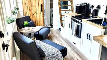 A compact kitchen with a stove, microwave, and sink. There is a wooden ladder leading to a lofted sleeping area.